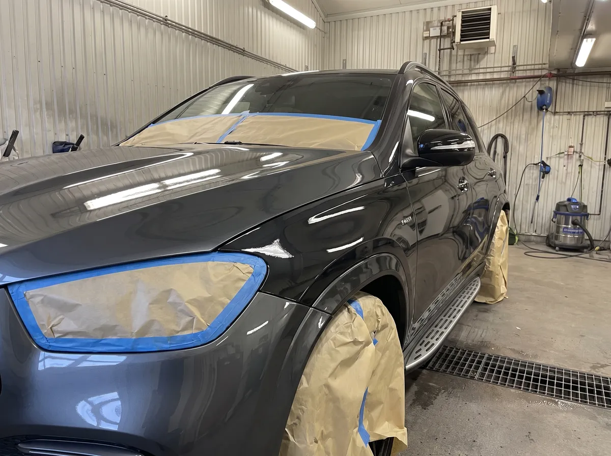 Mörk Mercedes-SUV avmaskerad med tejp och maskeringspapper över strålkastare och hjulhus, med nylackerad framskärm